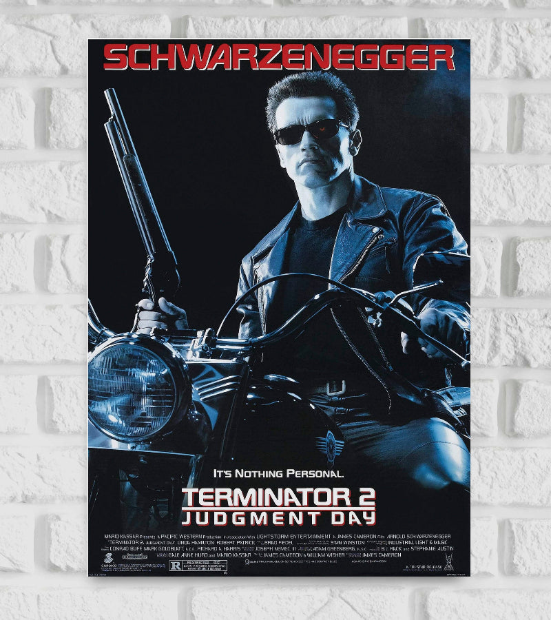 Poster of Hollywood Action Drama American science fiction The image shows the Terminator character wearing a black leather jacket and dark sunglasses sitting on a motorcycle holding a shotgun The background is dark and shadowy enhancing the film’s intense futuristic atmosphere At the top "SCHWARZENEGGER" is displayed in bold red text at the bottom the title "TERMINATOR 2 JUDGMENT DAY" appears in white and red, accompanied by the tagline “It’s Nothing Personal”