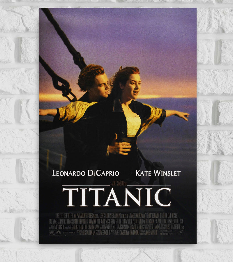 Poster of the movie 'Titanic' featuring the iconic scene of Jack (Leonardo DiCaprio) and Rose (Kate Winslet) standing at the bow of the ship, arms outstretched, with a sunset in the background. The names 'Leonardo DiCaprio' and 'Kate Winslet' appear above the title, and 'TITANIC' is written in large, bold white letters at the bottom