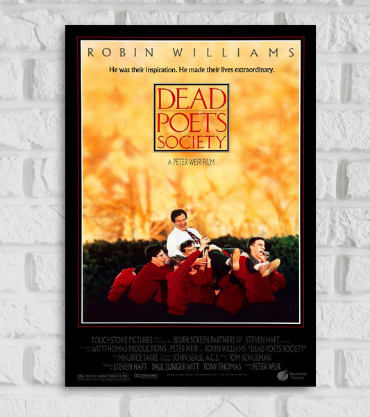 Poster from Hollywood film New England rouses The image shows a joyful scene where Robin Williams as the inspirational teacher Mr. Keating is being carried on the shoulders of a group of students dressed in red sweaters set against a warm golden background of autumn foliage At the top it reads “ROBIN WILLIAMS” and the tagline “He was their inspiration. He made their lives extraordinary” The film title “DEAD POETS SOCIETY” is prominently displayed in a red box at the center Todd Anderson Leonard Ethan Hawke