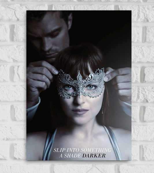 Poster for the romantic drama film "Fifty Shades Darker," a sequel in the Fifty Shades of Grey series. The image shows a close-up of a woman, Anastasia Steele, wearing an ornate silver masquerade mask Behind her Christian Grey is seen placing the mask gently on her face The background is dark and mysterious enhancing the intimate seductive mood At the bottom the tagline reads “SLIP INTO SOMETHING A SHADE DARKER” hinting at the film's deeper emotional and sensual theme Hollywood English erotic romance novel