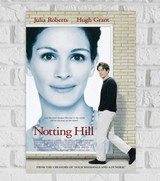 Poster of the romantic comedy film "Notting Hill" featuring Julia Roberts and Hugh Grant. The design shows a large black-and-white portrait of Julia Roberts in the background, looking serene. In the foreground, Hugh Grant walks past the portrait on a brick wall, looking toward the viewer. The tagline reads, "Can the most famous film star in the world fall for the man on the street?" The title "Notting Hill" is written in red serif font, and the top of the poster displays the names Julia Roberts Hugh Grant